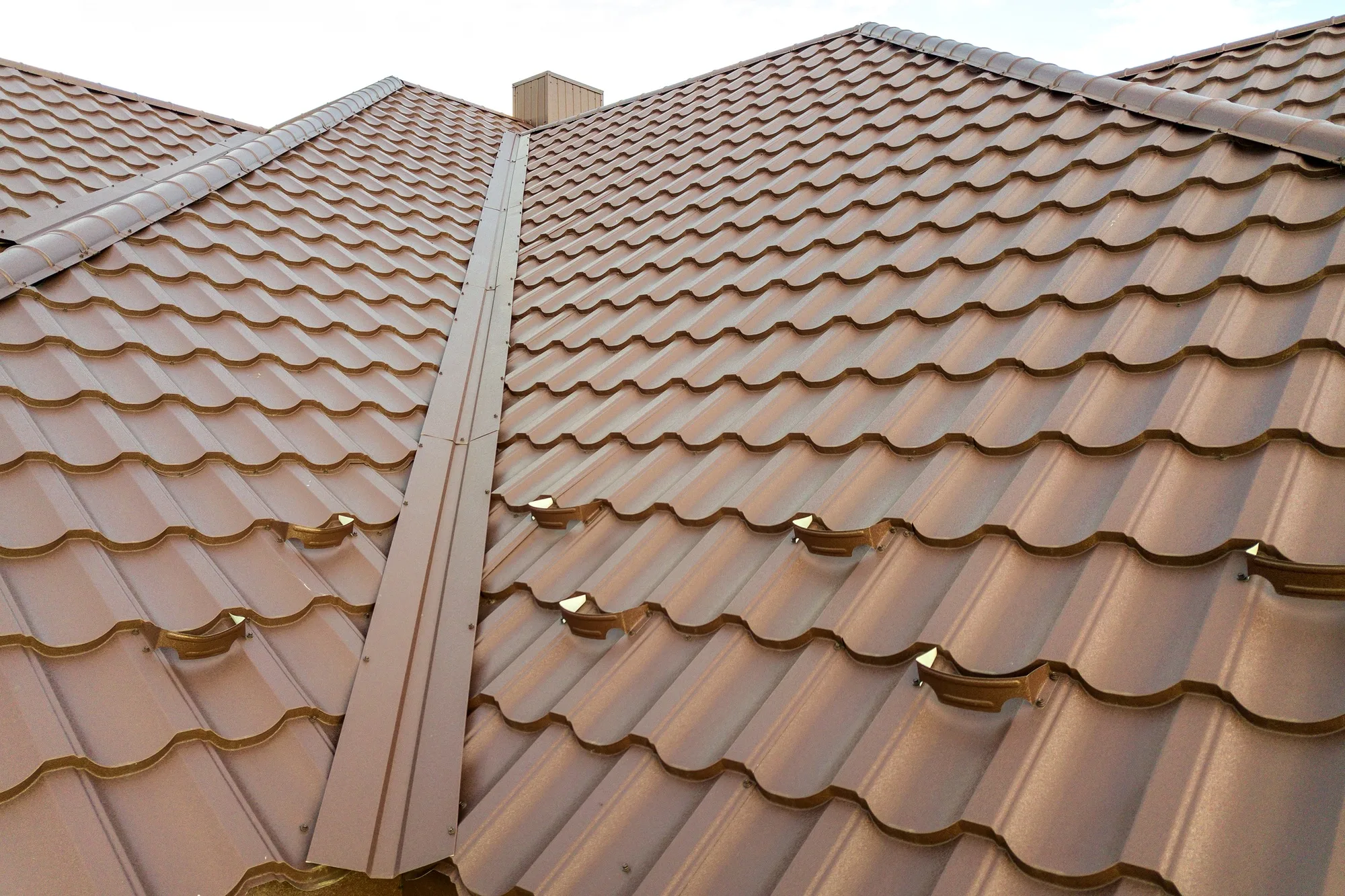 Detail of a house roof surface covered with brown metal tile sheets.